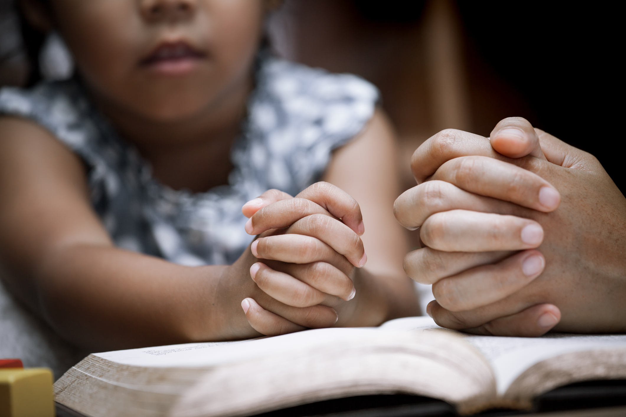 Mother and little girl hands folded in prayer on a Holy Bible together  for faith concept in vintage color tone